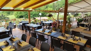 Un restaurante al aire libre con mesas y sillas, rodeado de vegetación.
