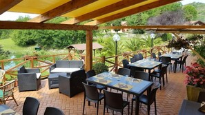 Un patio al aire libre con mesas y sillas, rodeado por una pérgola de madera y vistas a zonas verdes.