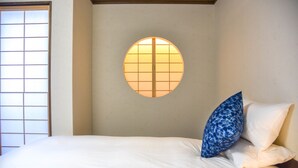 Ein Zimmer mit einem Bett, einem Fenster mit Gittermuster und einem runden Fenster mit Gittermuster an der Wand.