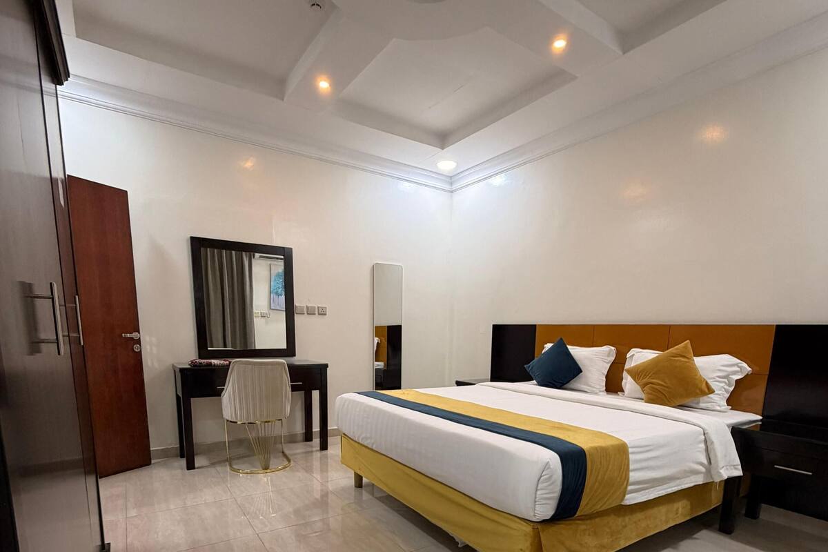 A hotel room with a large bed, a desk, a chair, a mirror, and a wardrobe.