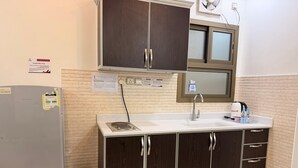 Una cocina con refrigerador, lavamanos, armarios y una ventana sobre la encimera.
