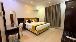 Habitación de hotel con cama, escritorio, silla, espejo, equipo de aire acondicionado y puerta.