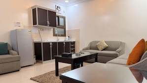 Un espacio habitable compacto con kitchenette, un sofá gris, una mesa de centro y una alfombra.