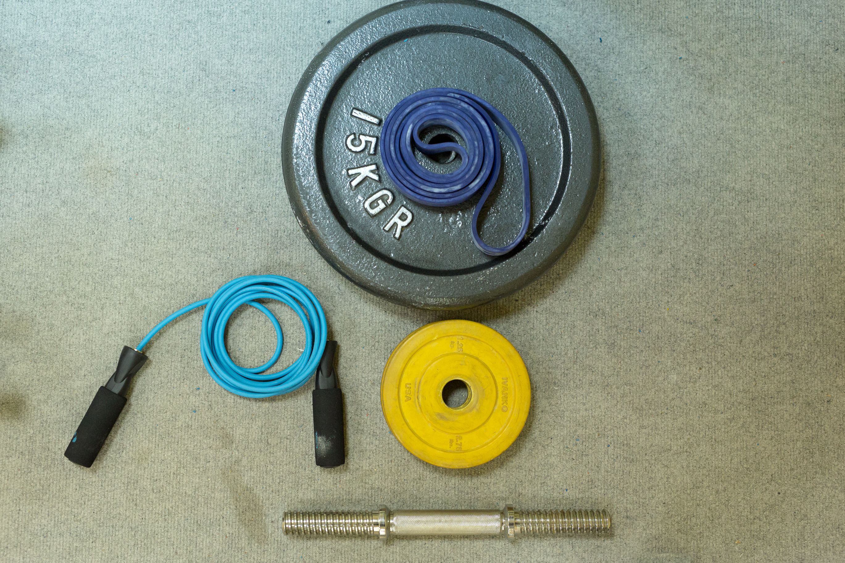 En viktplatta märkt med 15 KG, ett blått hopprep, en gul viktplatta och en skivstång av metall.