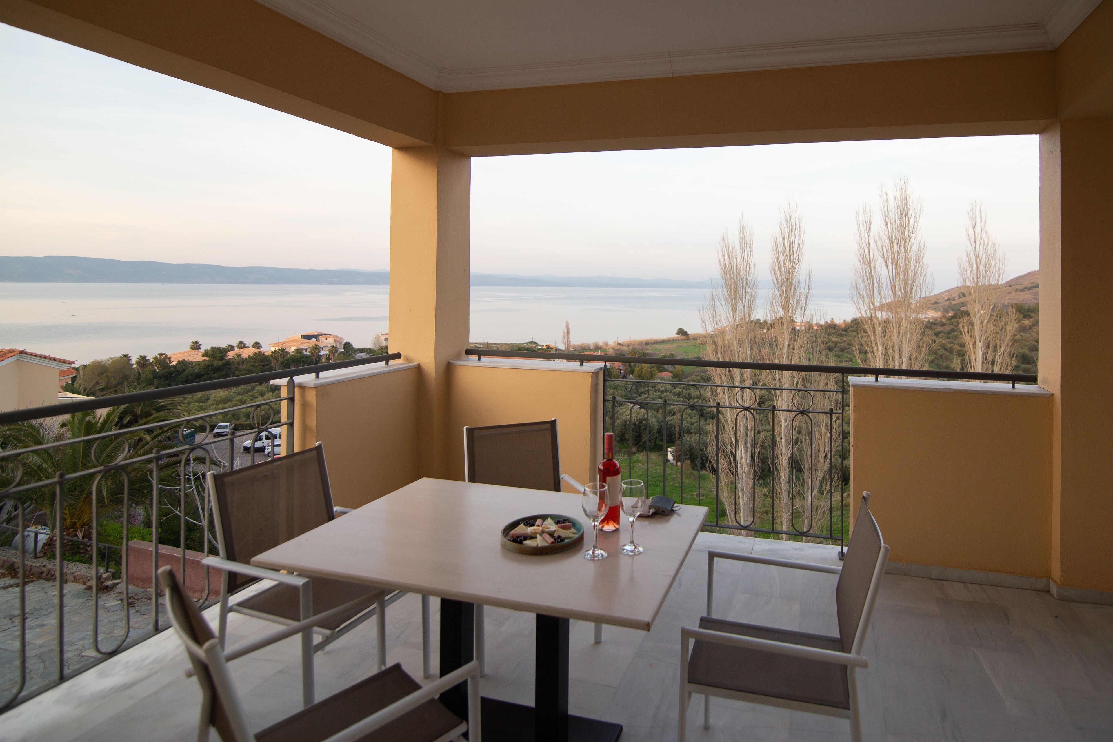 A balcony with a table and chairs, overlooking a body of water and distant land.