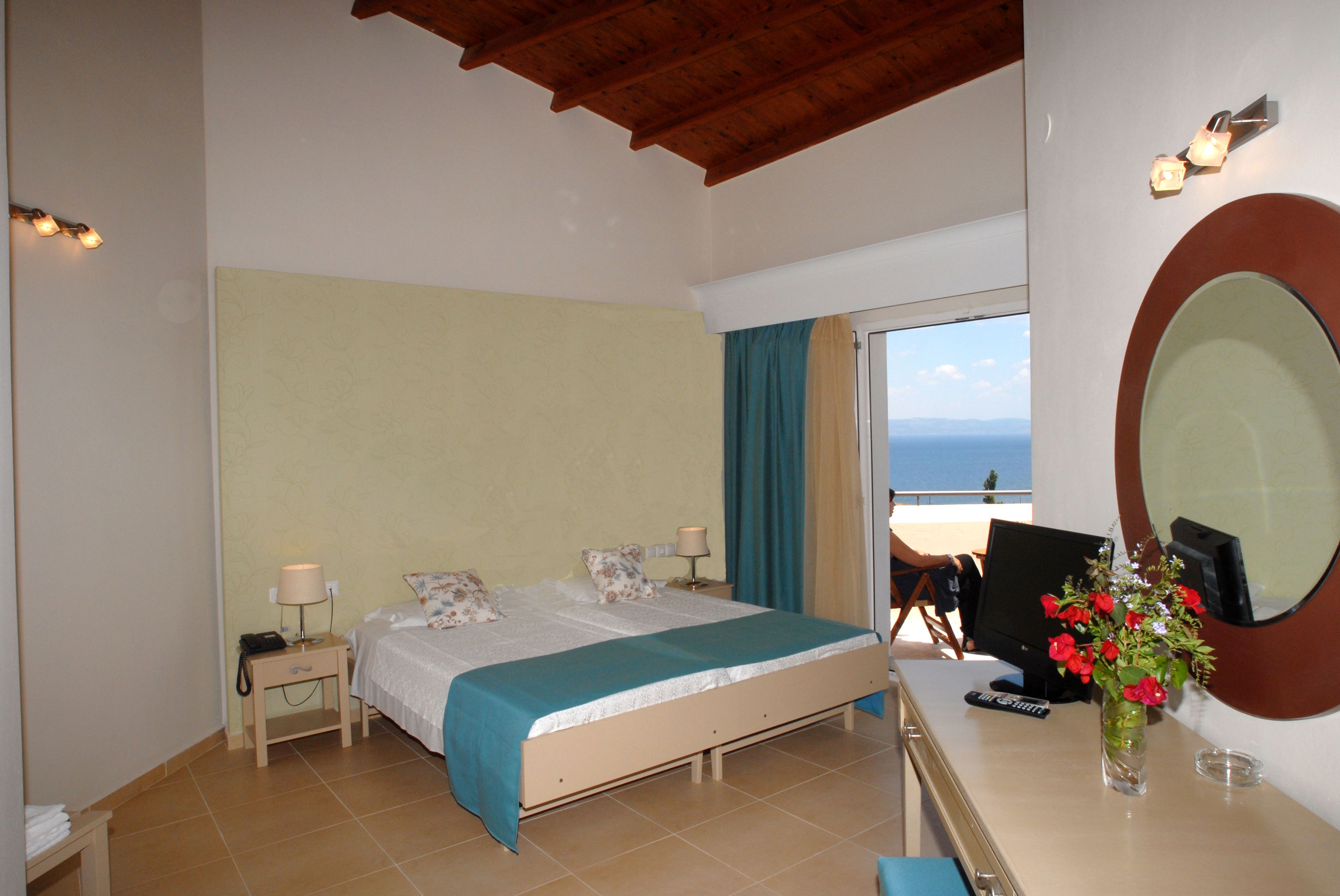 A bedroom with a bed, bedside tables, a desk with a computer, a vase with flowers, and a large mirror.
