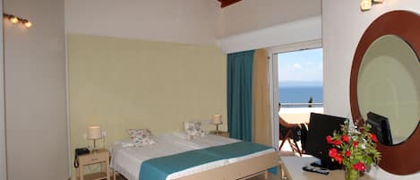 A bedroom with a bed, bedside tables, a desk with a computer, a vase with flowers, and a large mirror.