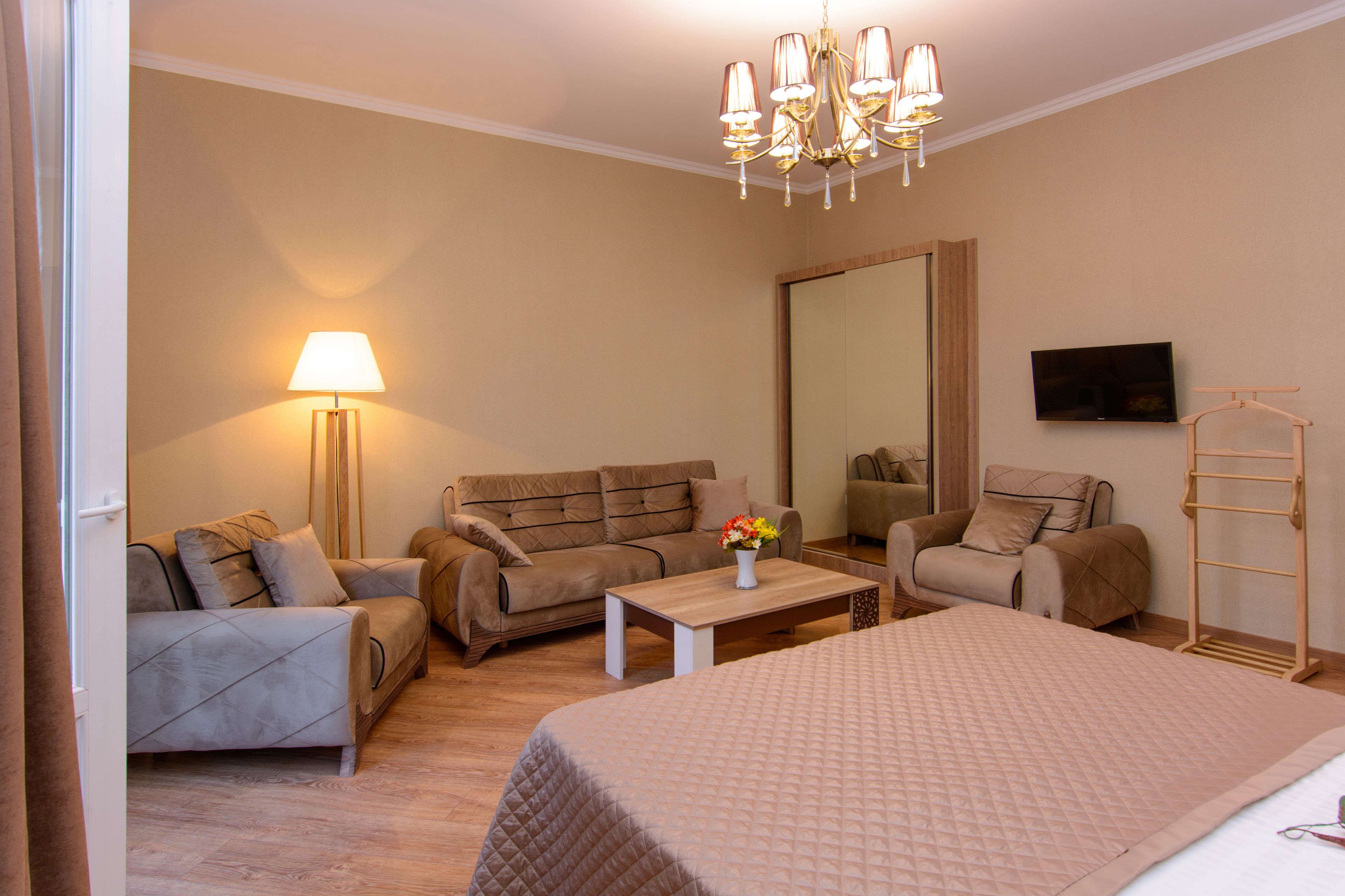 A hotel room with a bed, two sofas, a coffee table, a lamp, a TV, and a mirror.