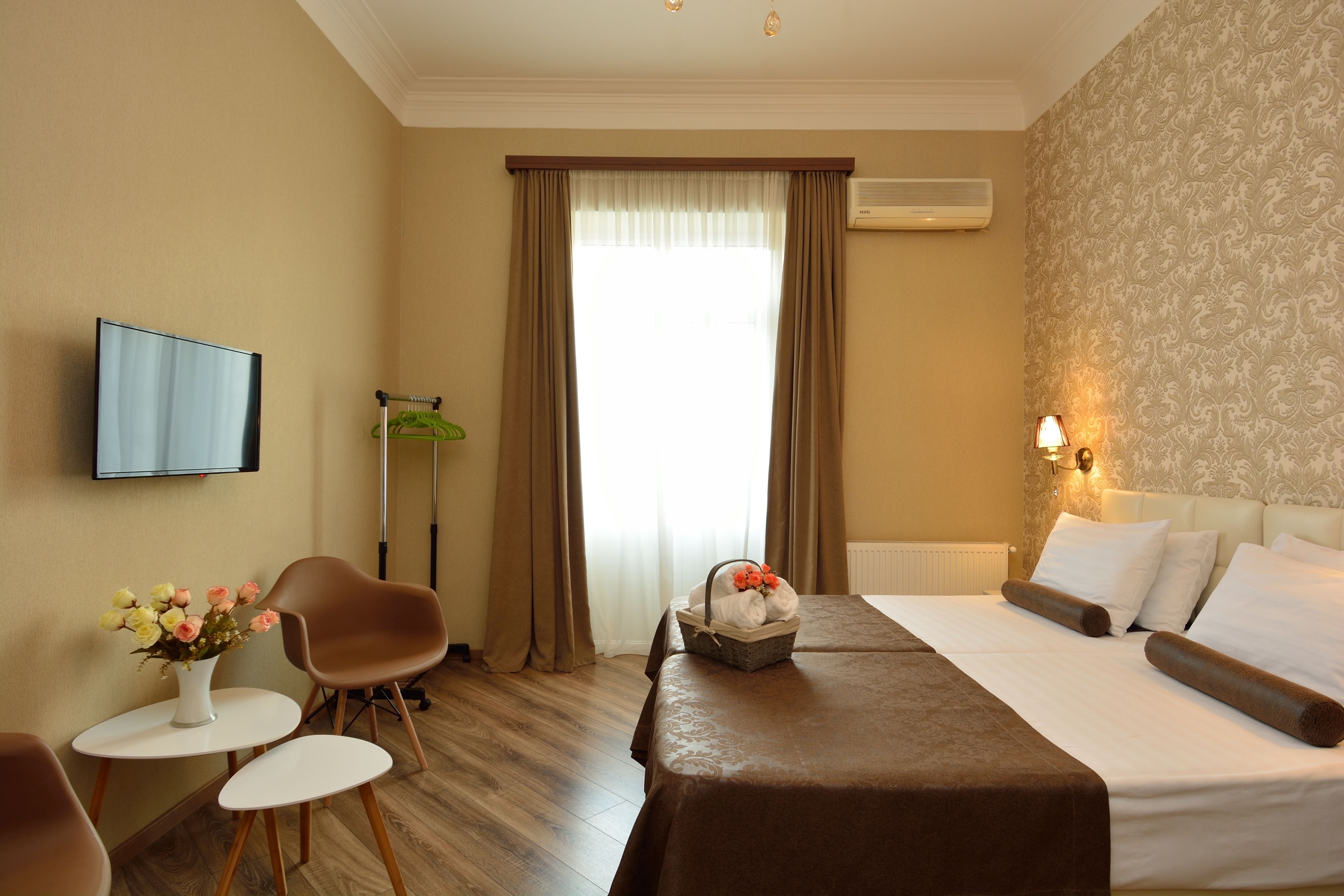 Hotelkamer met een bed, televisie, bureau met een bloevas en raam met gordijnen.
