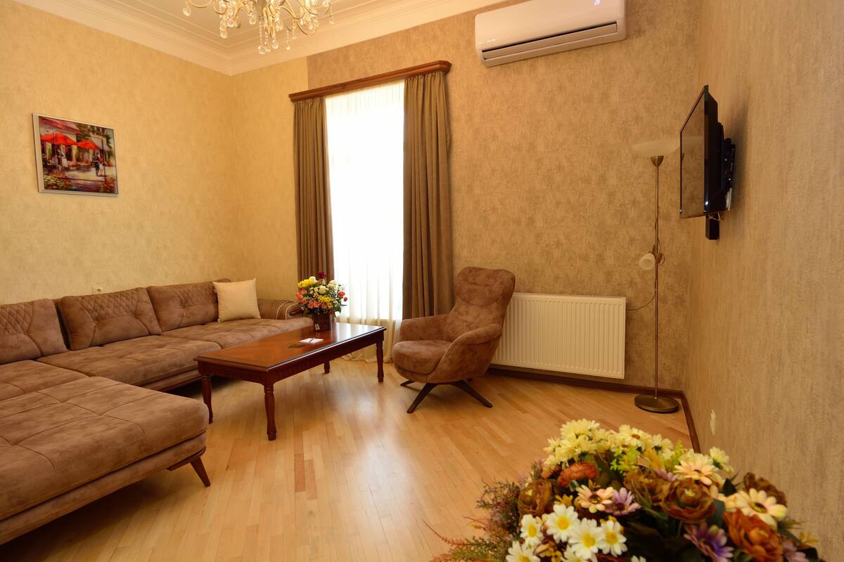 A living room with a sectional sofa, a single armchair, a wooden coffee table, and a floral arrangement.