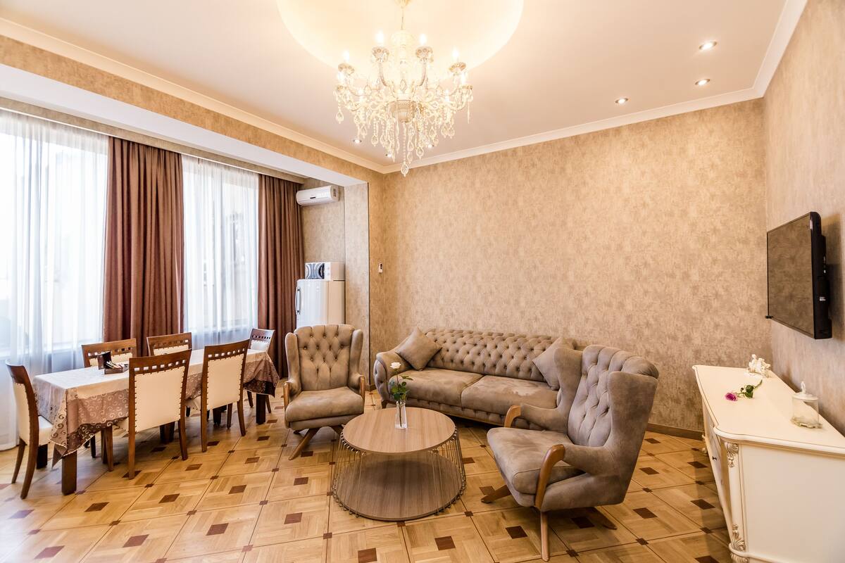 A spacious living room with a large sofa, a dining table with chairs, a round coffee table, and a chandelier.