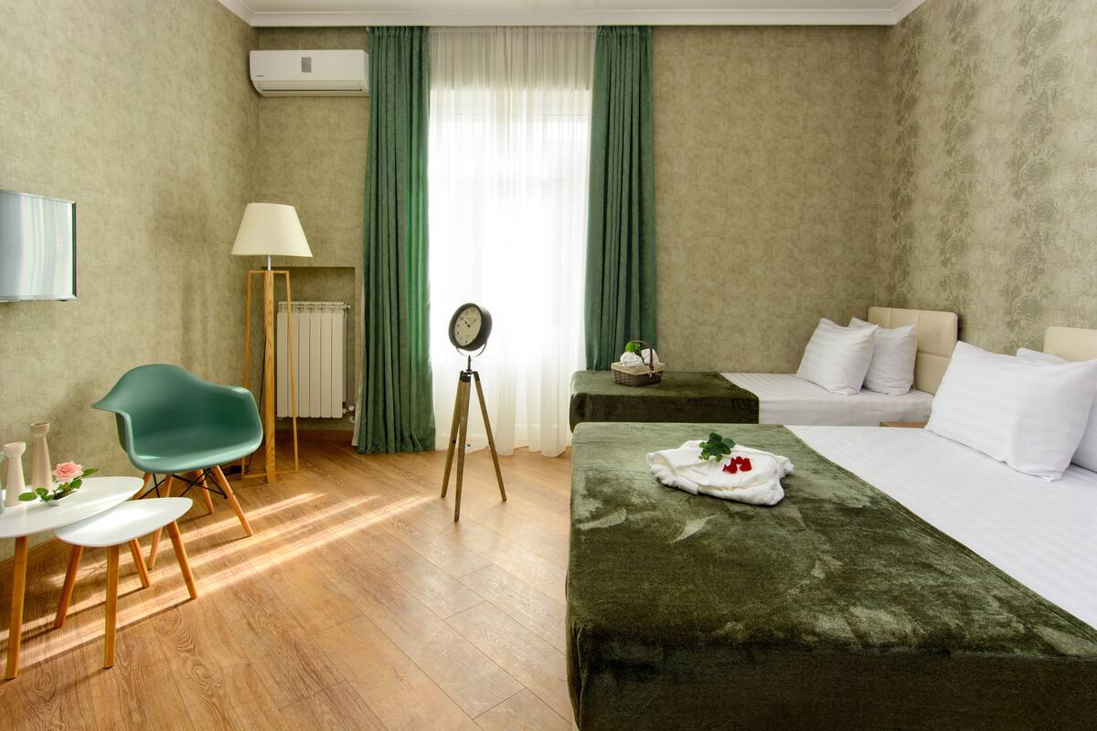 A hotel room with a bed, a desk, a chair, a lamp, a clock, and a mirror.