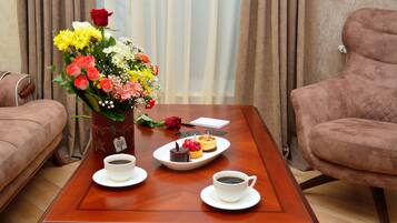 A wooden coffee table with two cups of coffee, a plate with desserts, and a bouquet of flowers.