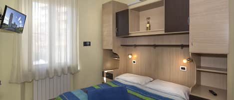 Un dormitorio con cama, televisor, ventana con cortinas y estanterías empotradas.