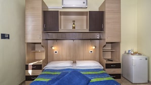 A bedroom with a bed, a small refrigerator, and built-in wooden cabinets. - Affittacamere Elisa (Pisa)