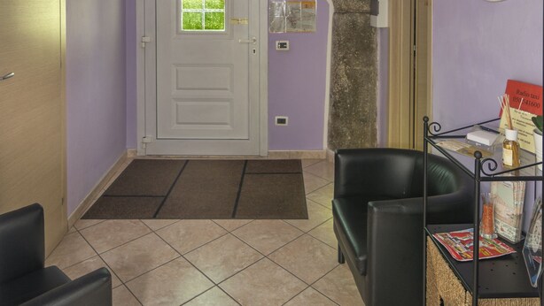 A hallway with a white door, a black leather chair, a small table with magazines, and a tiled floor. - Affittacamere Elisa (Pisa)