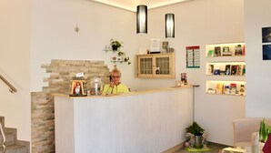A reception desk with a person behind it, a stone wall, a wooden cabinet, and shelves with books and decorative items. - Pension Alscher (Goslar)