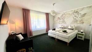 A modern hotel room with a bed, a small desk, a chair, a potted plant, and a large window with curtains. - Pension Alscher (Goslar)