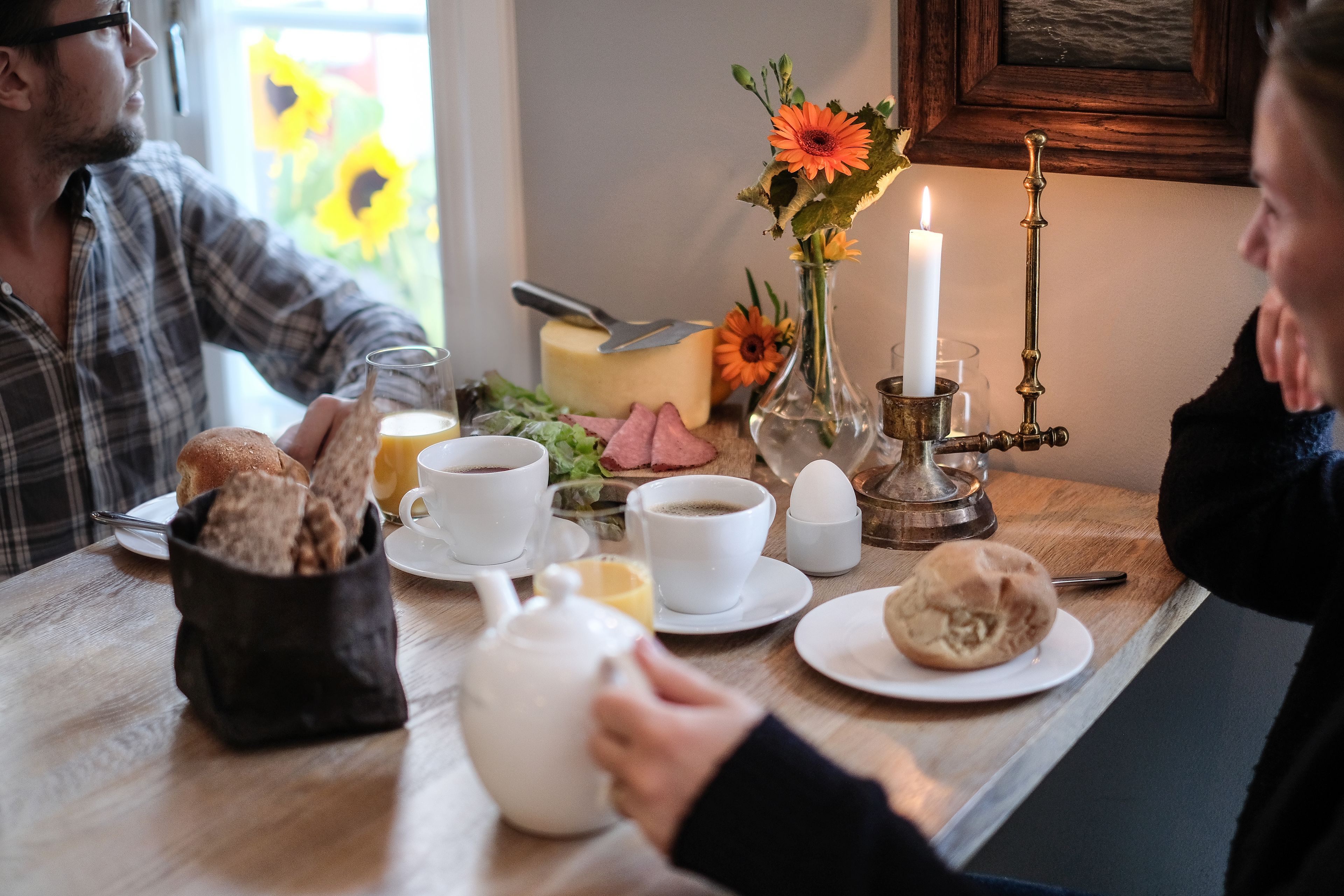 Ein Frühstückstisch mit Tellern, Tassen, einem Teekessel und einer Kerze.