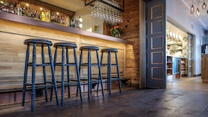 Una zona de bar con taburetes de madera, una estantería llena de botellas y una vitrina de cristal.