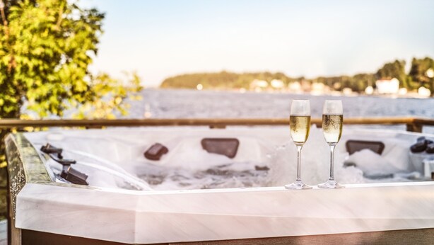Un jacuzzi con dos copas de champán, rodeado de hielo, con vista a un cuerpo de agua y árboles al fondo.