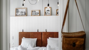 Habitación de hotel con una cama blanca, dos almohadas, un cabecero marrón y una bolsa marrón colgando.
