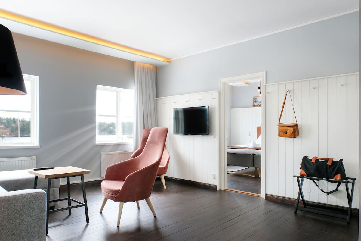 A modern room with a wooden floor, a grey sofa, a pink chair, a small table, a TV mounted on the wall, a white wardrobe, and a hanging bag.