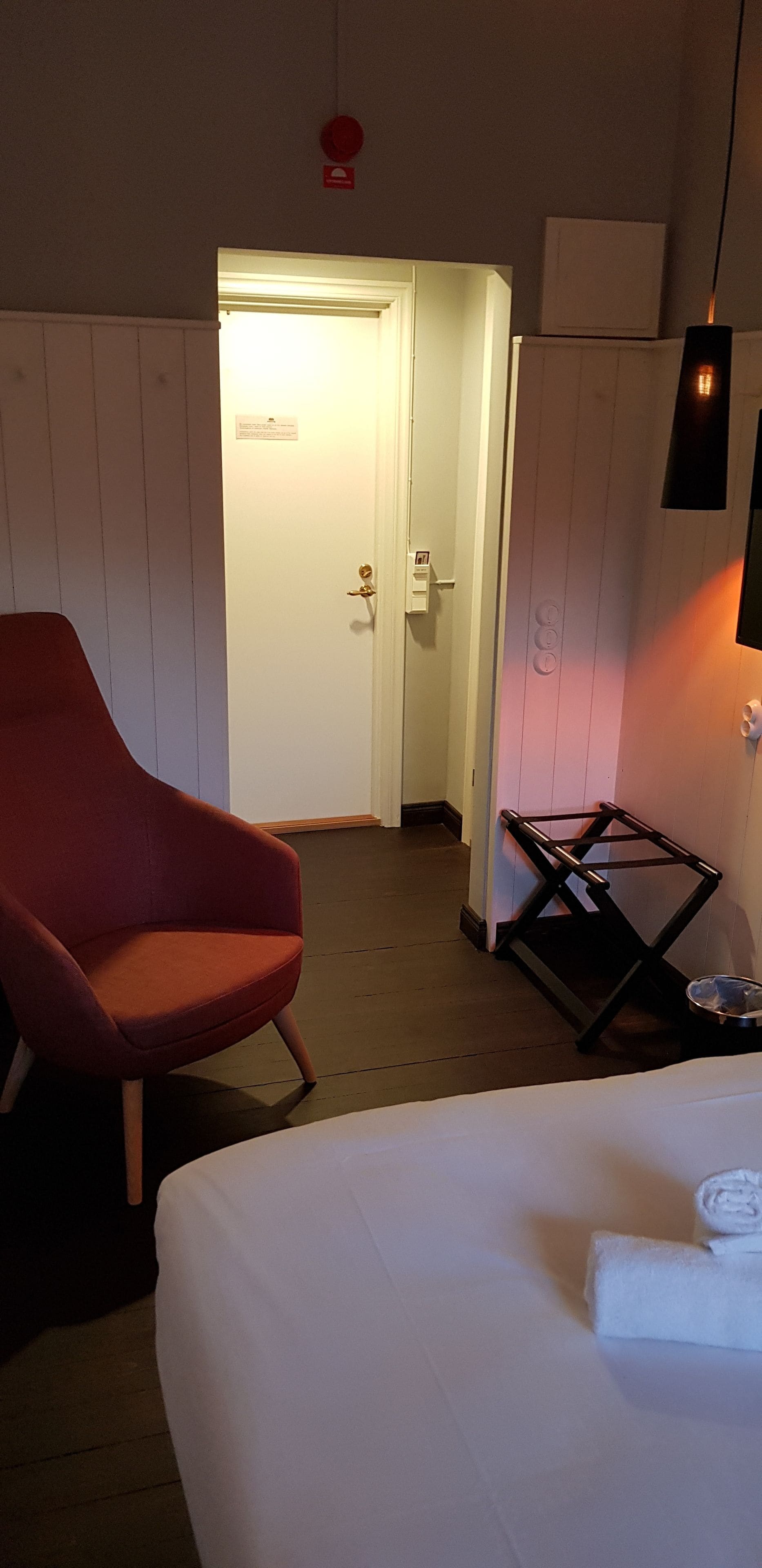 A hotel room with a bed, a red chair, a small table, and a door leading to another room.
