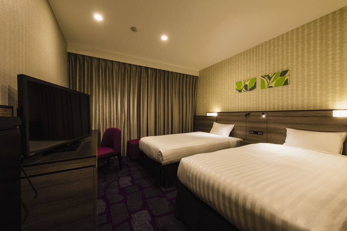 A hotel room with two beds, a TV, a desk, and a chair.