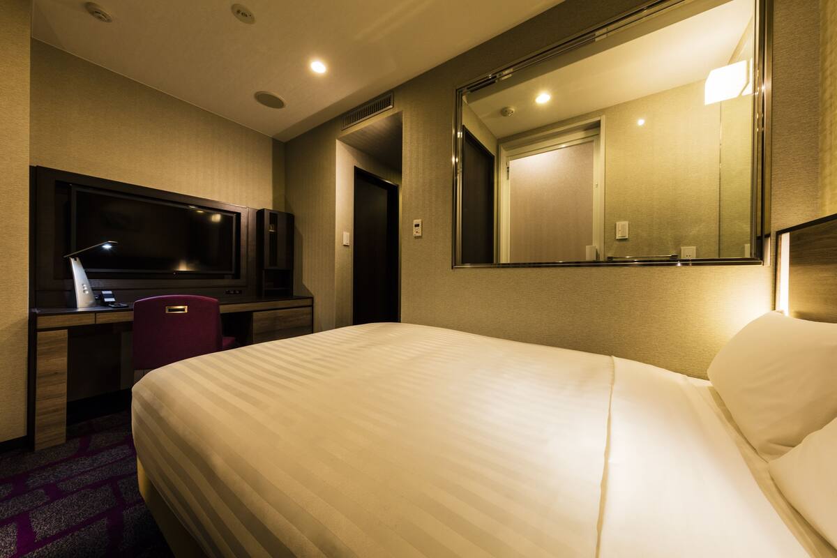 A hotel room with a large bed, a desk with a television, a chair, and a mirror.