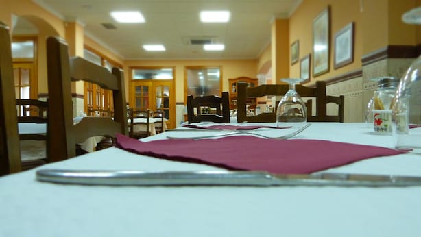 A dining area with tables set for two, wooden chairs, and a white tablecloth. - Hostal La Masía (Villarreal)