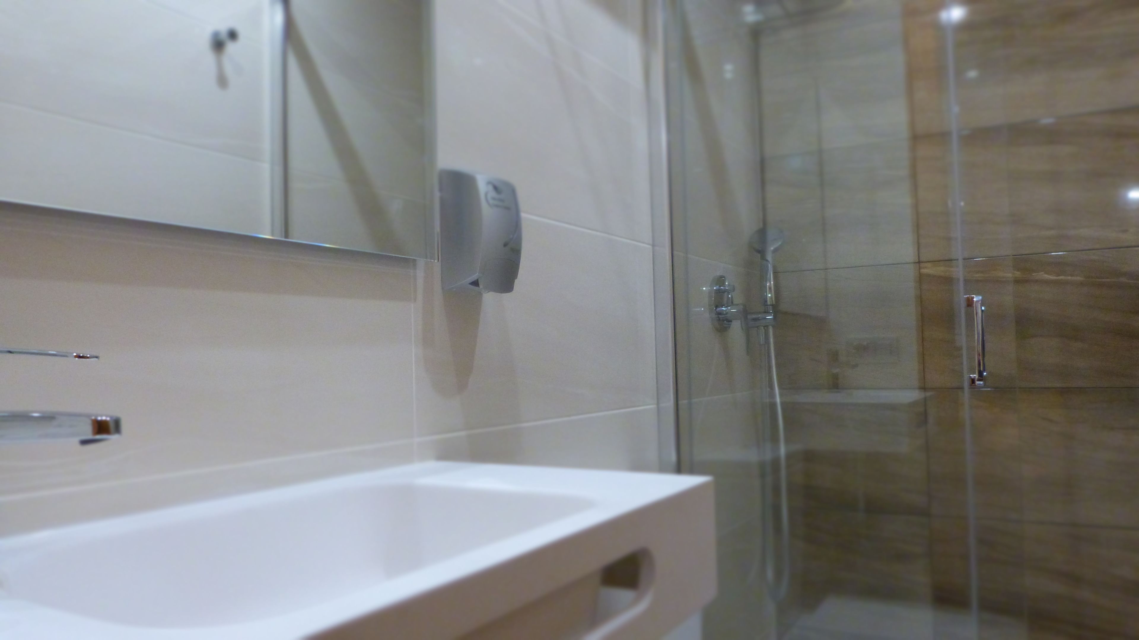 Een moderne badkamer met een douchecabine van glas, een wit wastafelmeubel en een spiegel met een zeepdispenser.
