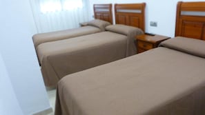 Una habitación de hotel con dos camas individuales, cabeceros de madera, una mesita de noche y una ventana con persianas.