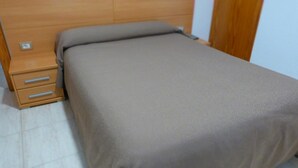 A bedroom with a bed, a wooden nightstand with drawers, and a light switch on the wall. - Hostal La Masía (Villarreal)