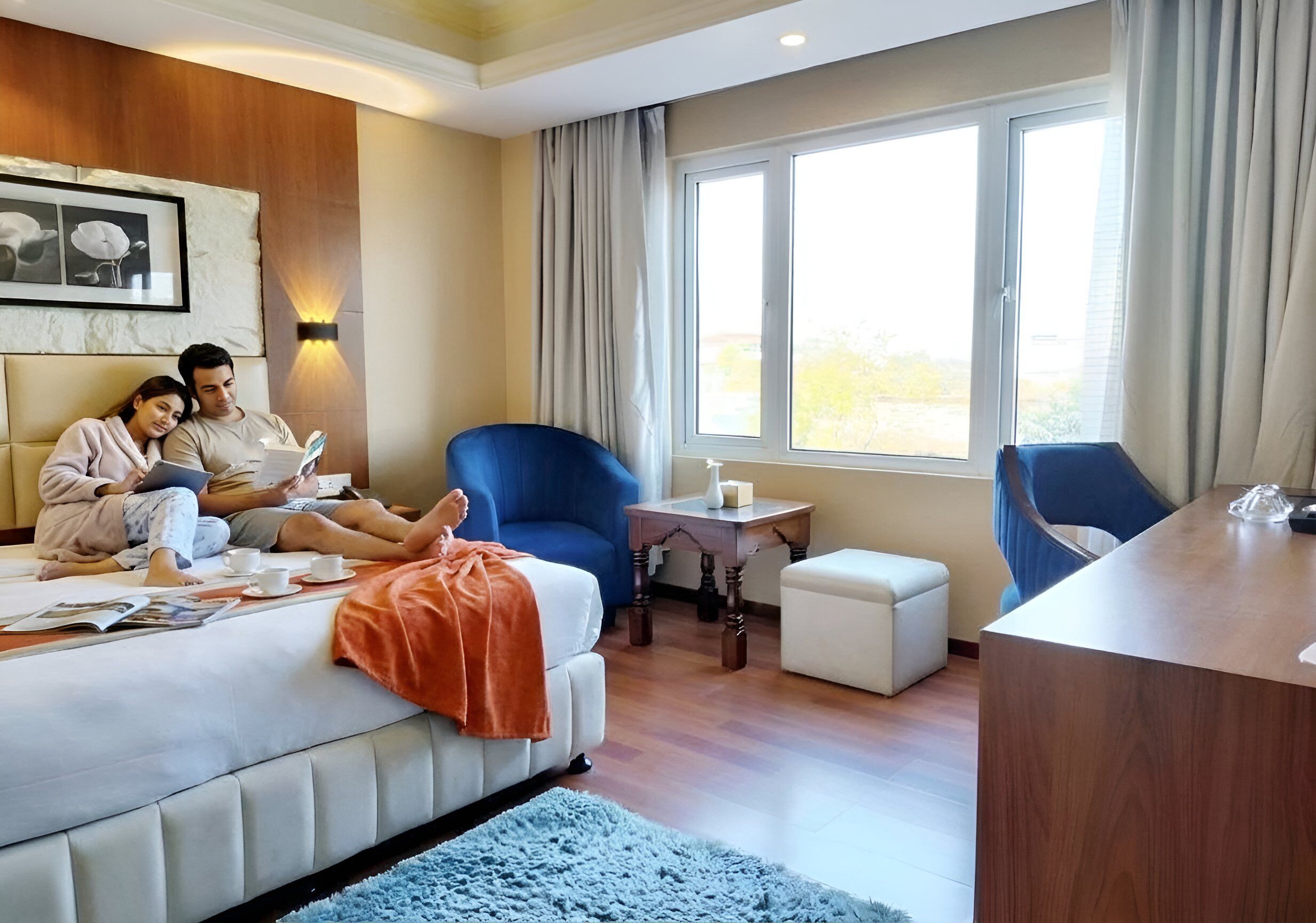 Ein Hotelzimmer mit einem Bett, einem blauen Sessel, einem kleinen Tisch mit Kerze sowie einem Schreibtisch.
