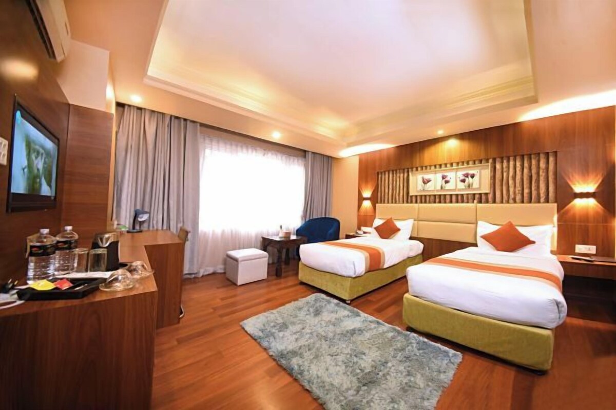 A hotel room with two beds, a desk, a chair, a small table, and a TV.