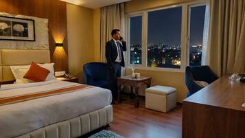Habitación de hotel con cama, escritorio, silla y vista a la ciudad de noche.