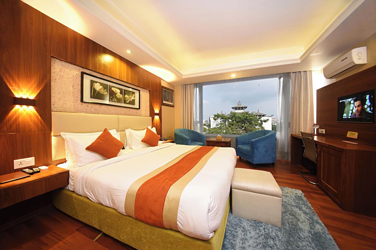 Une chambre d’hôtel avec un grand lit, un bureau, une télévision et une vue sur une tour.