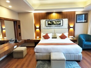 A hotel room with a large bed, a wooden headboard, a desk with a mirror, and a blue armchair.