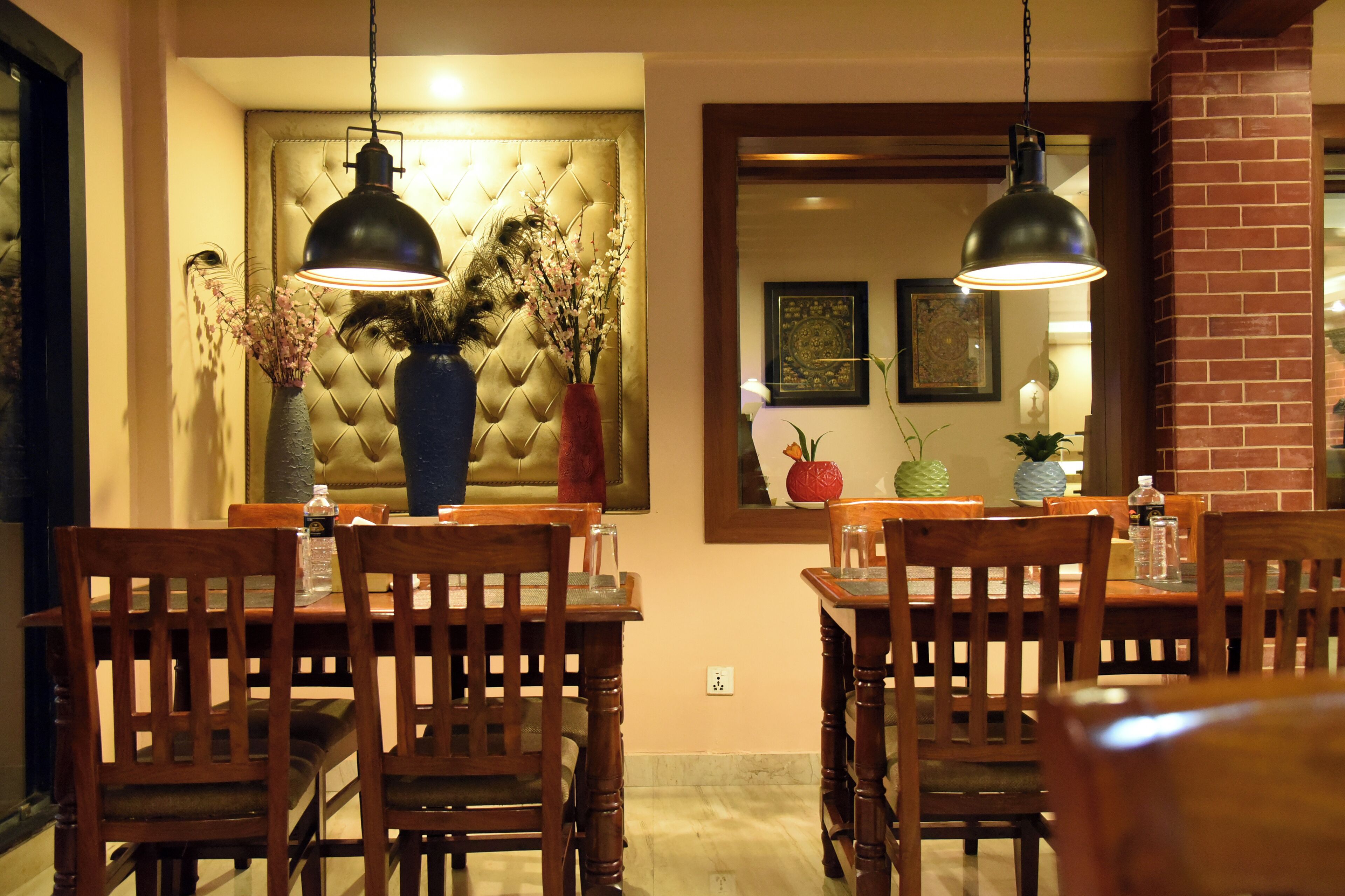 A dining area with wooden chairs and tables, a tufted headboard, and pendant lighting.
