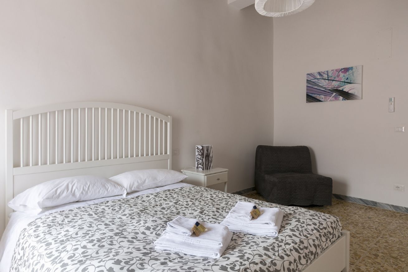 Un lit bien fait, avec une couvre-lit à motifs, une tête de lit blanche et deux serviettes pliées posées sur le lit.