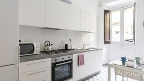 Eine moderne Küche mit weißen Schränken, einem Gasherd, einer Mikrowelle und einem Toaster. Ein Fenster bietet Blick ins Freie.