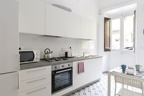 Eine moderne Küche mit weißen Schränken, einem Gasherd, einer Mikrowelle und einem Toaster. Ein Fenster bietet Blick ins Freie.