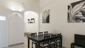 Ein Essbereich mit einem rechteckigen Tisch, sechs Stühlen, einem Fernseher auf einem Schrank und drei abstrakten Wandbildern.
