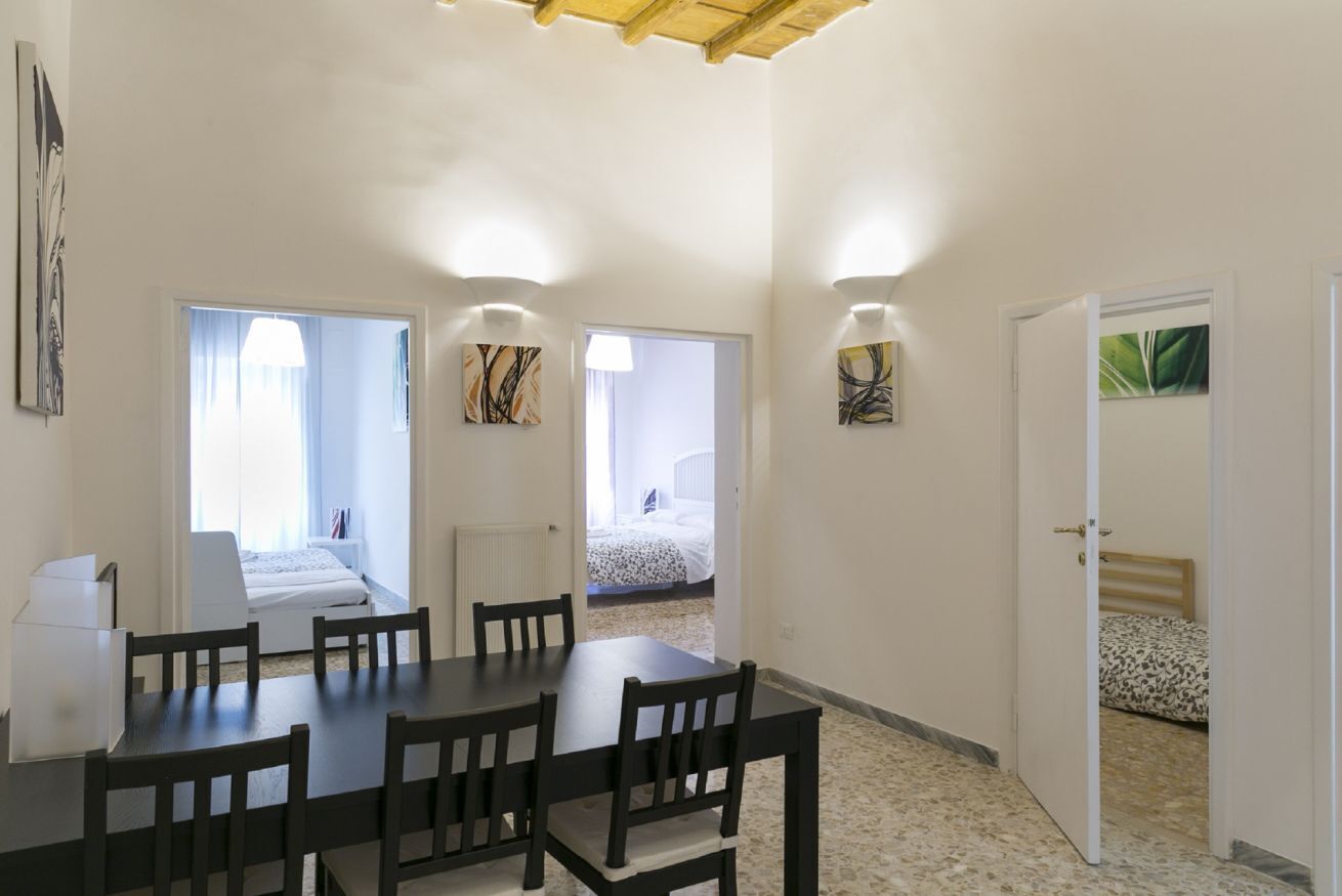 A dining area with a table and chairs, two windows with curtains, and a door leading to a bedroom.