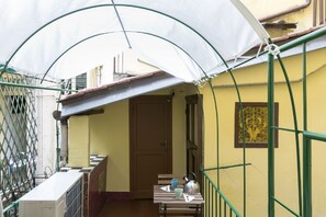 Un pequeño balcón con un toldo blanco, una mesa de madera con una tetera, tazas y una silla.