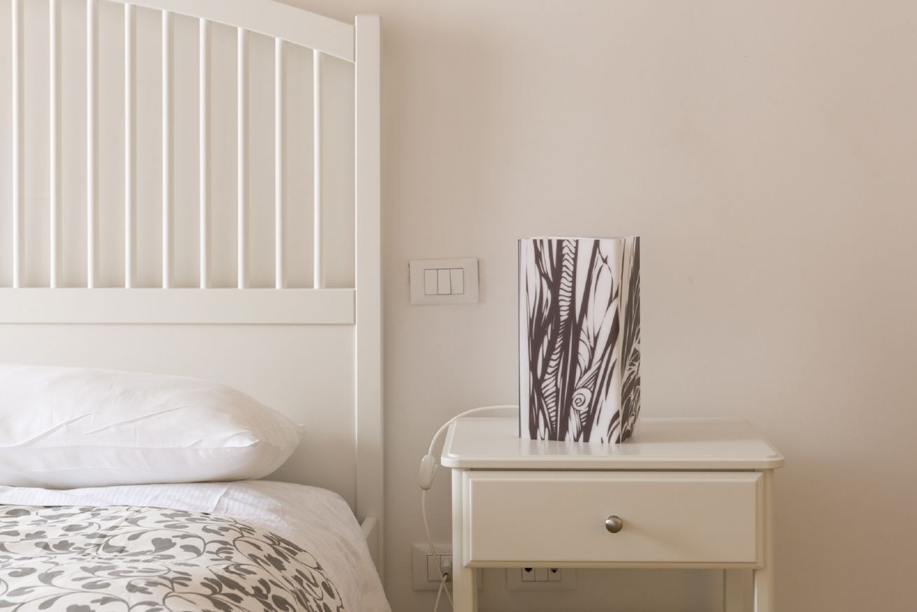 A bedroom with a bed, a nightstand, and a wall-mounted light switch.