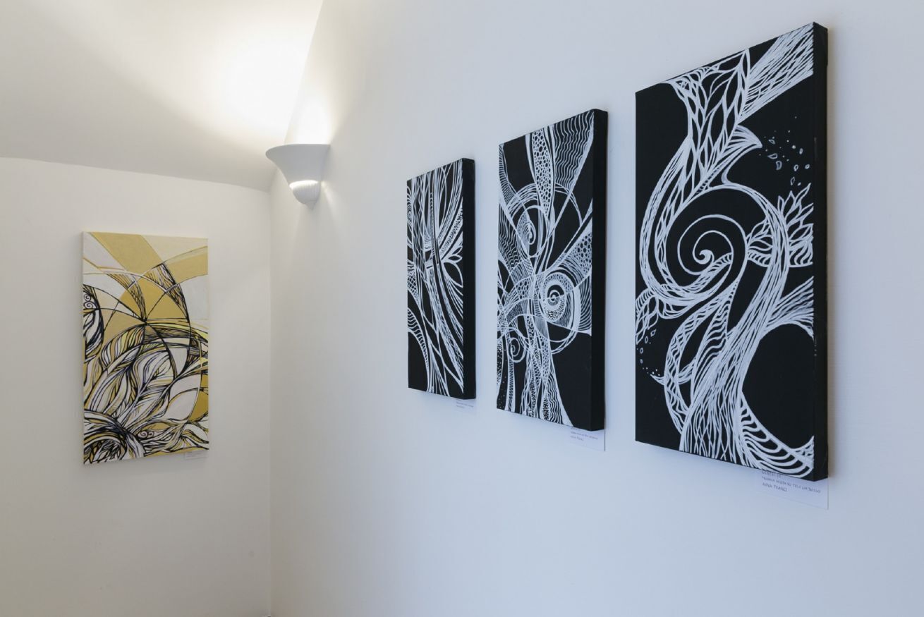 Three abstract paintings on a white wall in a gallery setting.