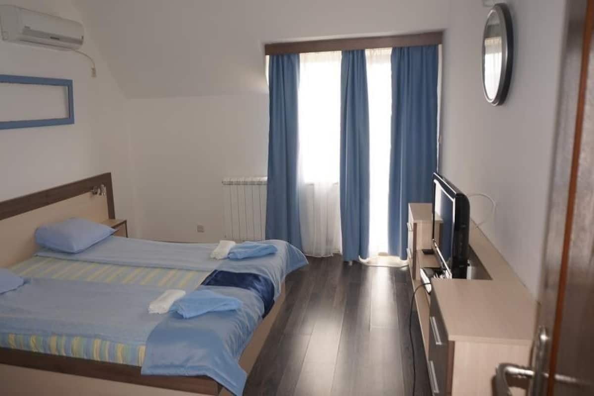 Ein Hotelzimmer mit zwei Betten, einem Schreibtisch, einem Fernseher und einem Fenster mit Vorhängen.