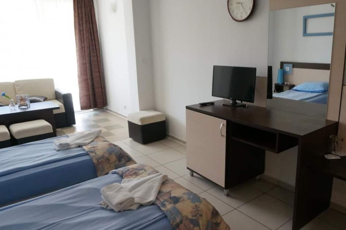 Ein Hotelzimmer mit zwei Betten, einem Schreibtisch mit Fernseher, einer Sitzecke und einem großen Spiegel.